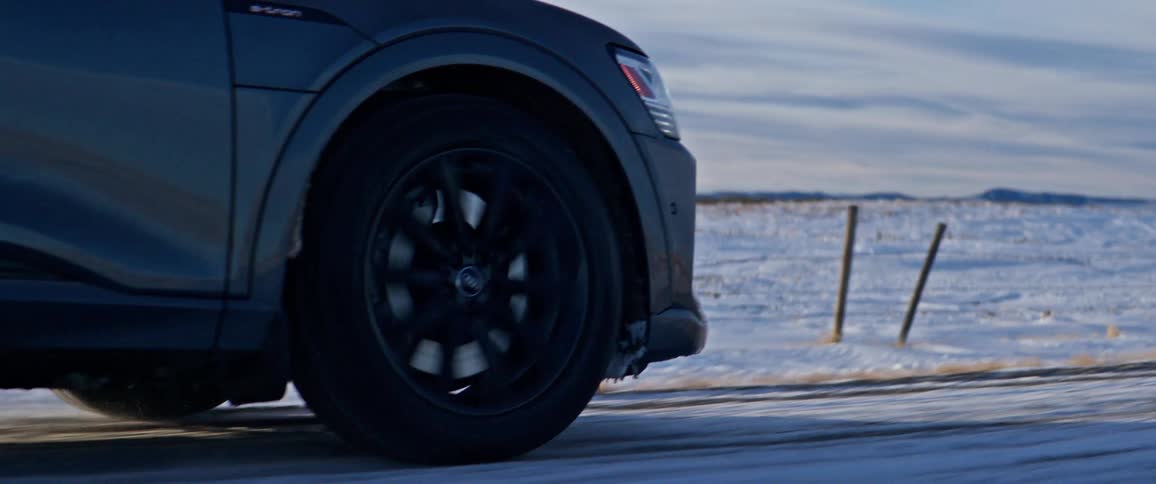 A vehicle driving on a snowy road with a snowy landscape the sky and clouds in the background