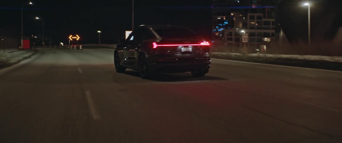 A sedan turns onto a city highway at night and speeds off