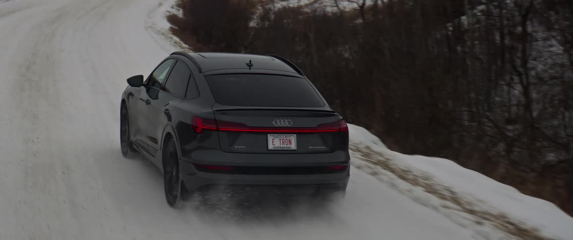 A black crossover vehicle drives on a curved snow covered road