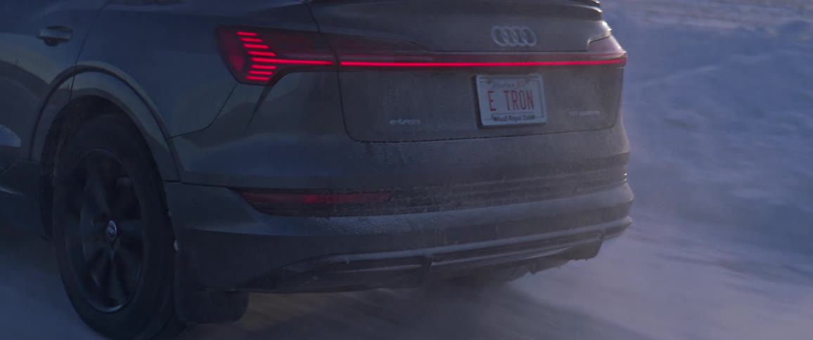 A black audi car is driving on a road during snowy season