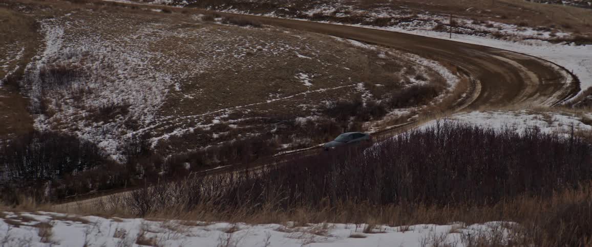 Dark grey audi car drives downhill on snowy dirt road