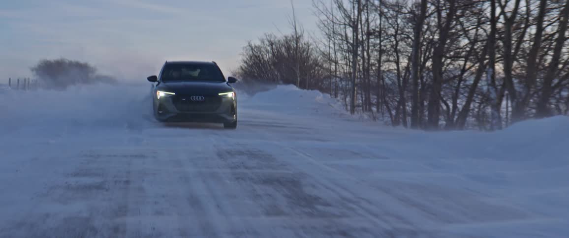 A vehicle driving on a snowy road with trees the sky and clouds in the background