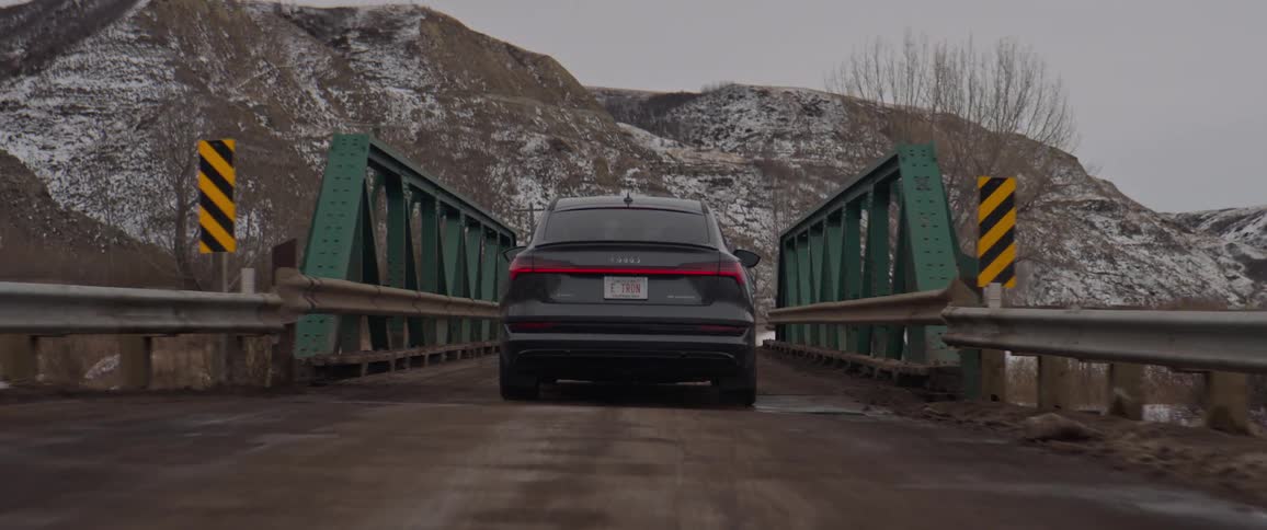 A vehicle driving on a bridge with a mountain range the sky and clouds in the background