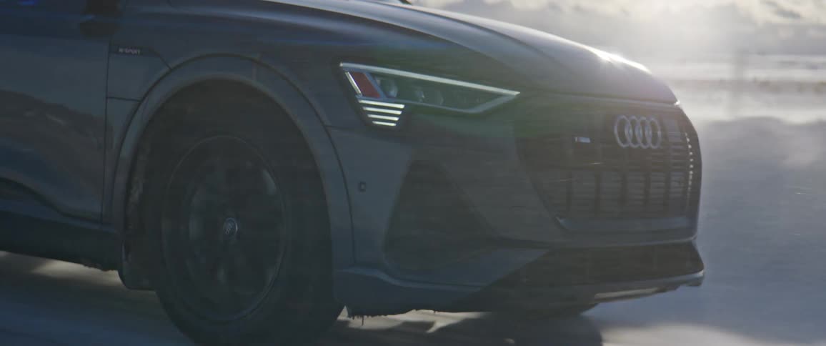 Dark audi car drives on snowy dirt road in the field