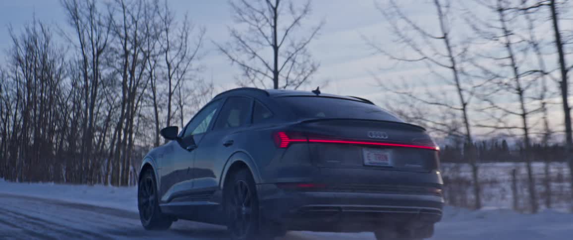 A vehicle driving on a snowy road with trees the sky and clouds in the background