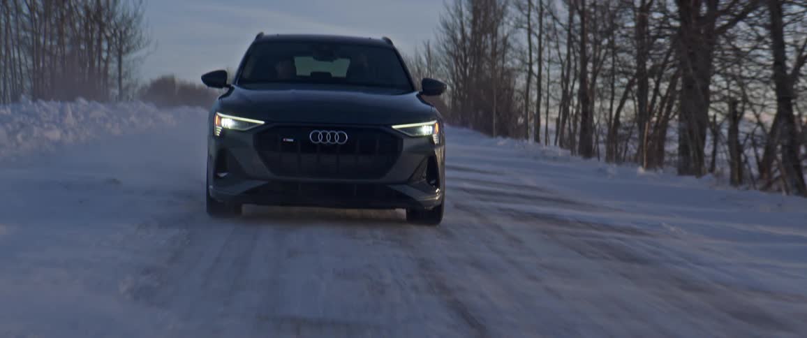 A vehicle driving on a snowy road with trees the sky and clouds in the background