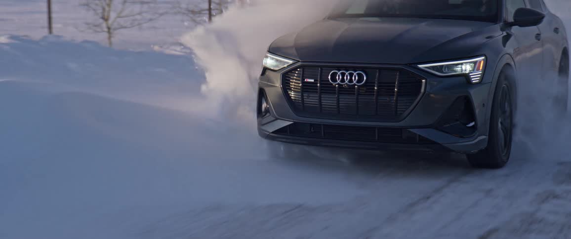 A black audi automobile travels on a snow covered road
