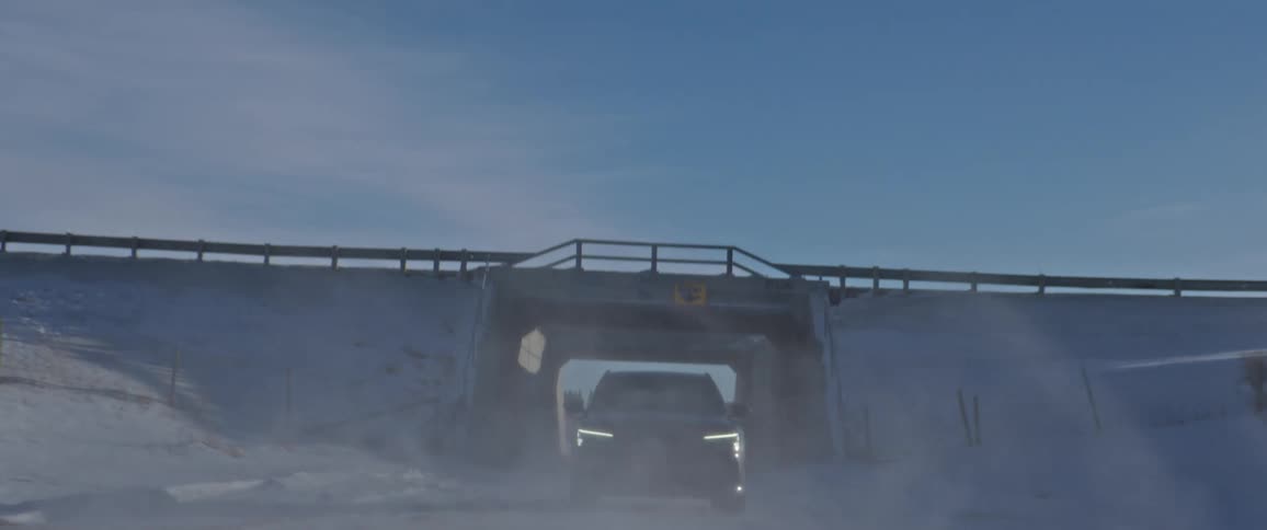 A black car travels through an underpass on a snow covered road