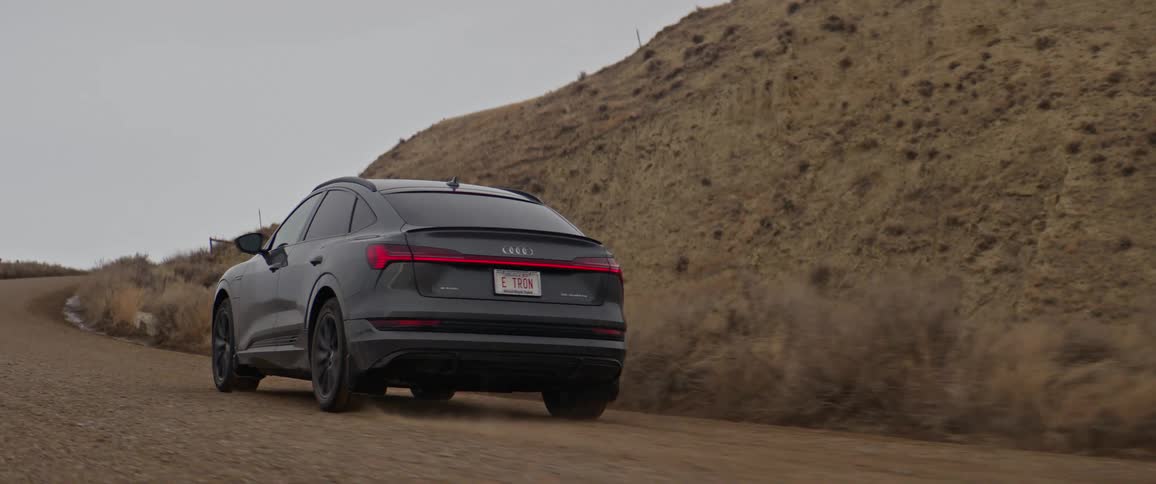 A vehicle driving on a dirt road with a hill the sky and clouds in the background