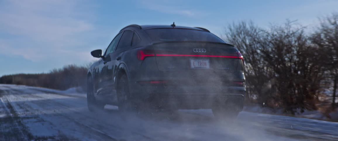 A vehicle driving on a snowy road with trees the sky and clouds in the background