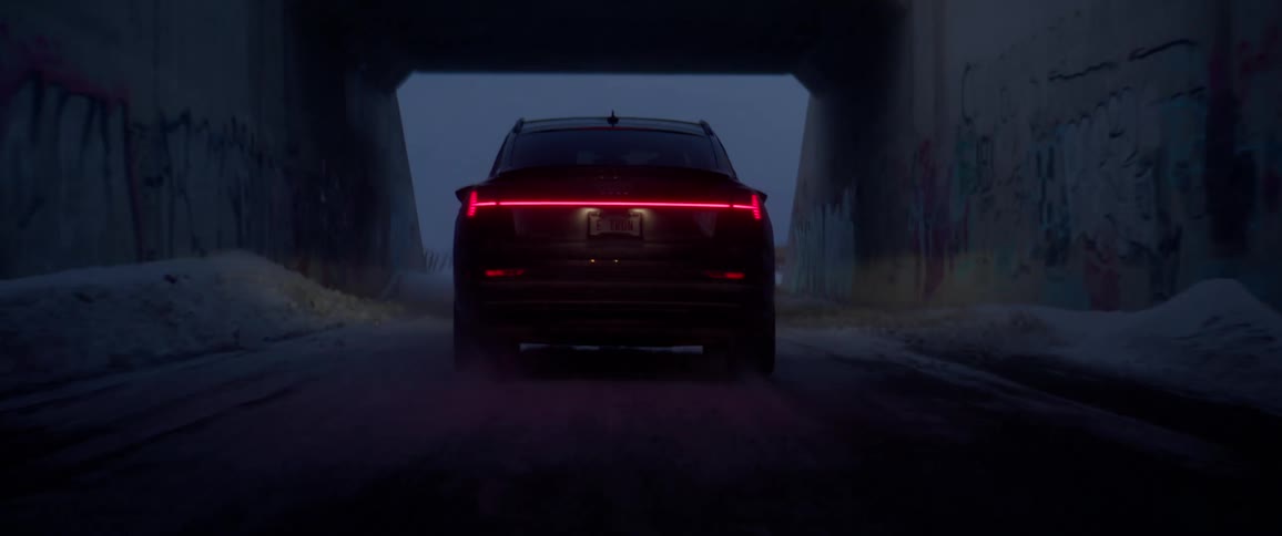 A black car travels through an underpass on a snow covered road