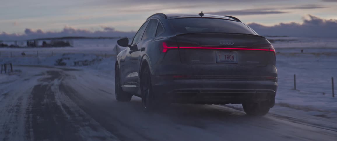A car drives on road in a rural area next to a snow covered field