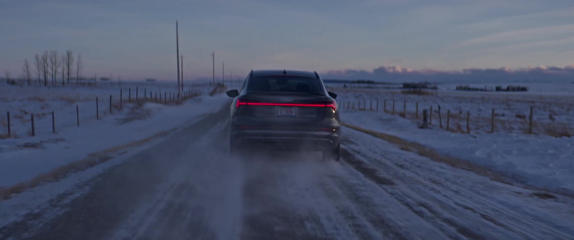 Dark gray audi car drives on snowy dirt road in the field at dusk