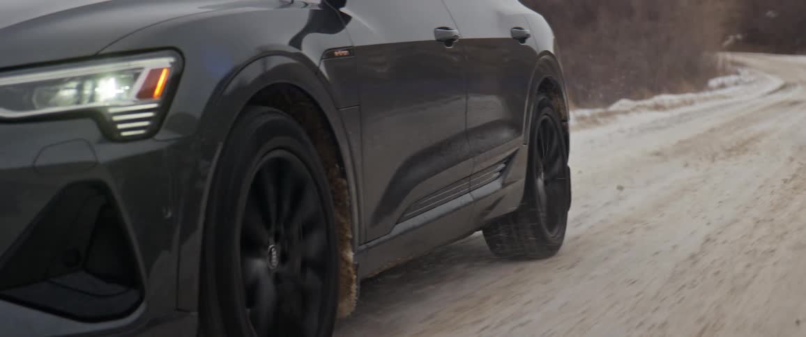 Dark gray audi car drives on dirt road with snowy hills in the background