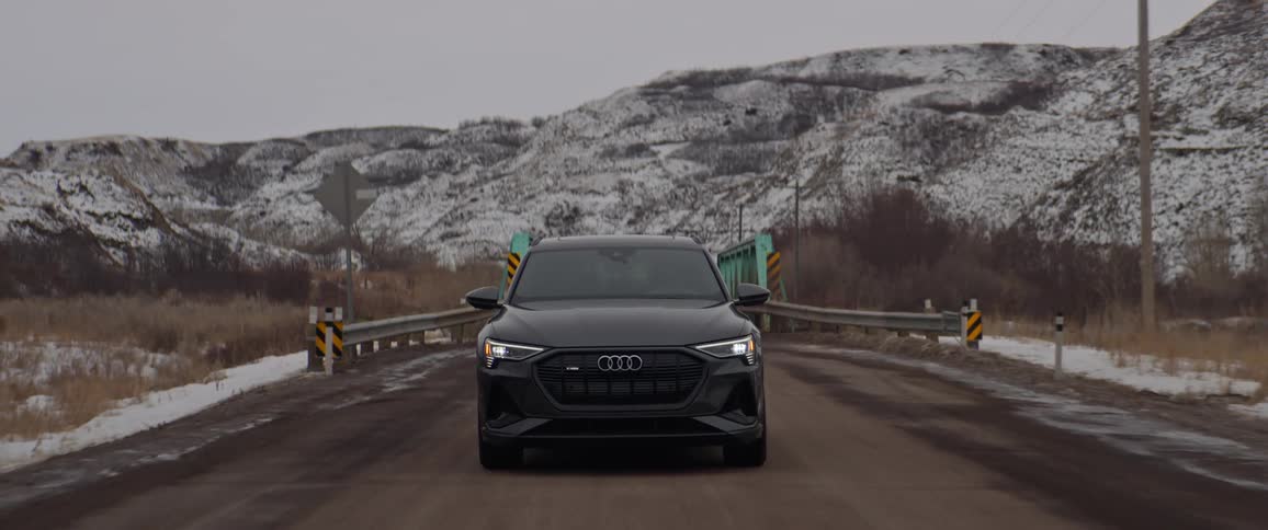 A vehicle driving on a bridge with a mountain range the sky and clouds in the background