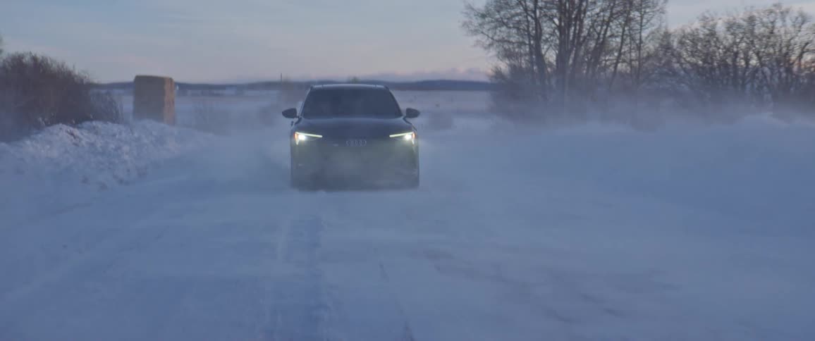 A vehicle driving on a snowy road with the sky and clouds in the background