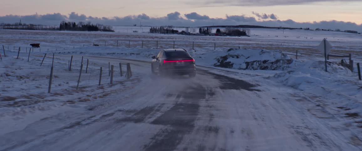 A vehicle driving on a snowy road with trees the sky and clouds in the background
