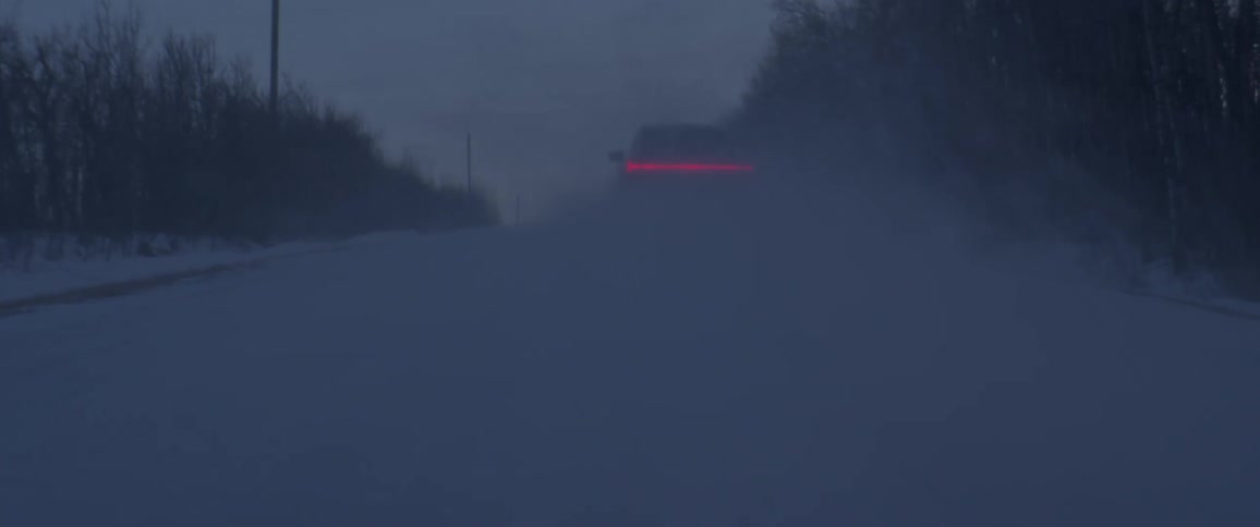 A vehicle driving on a snowy road with the sky and clouds in the background