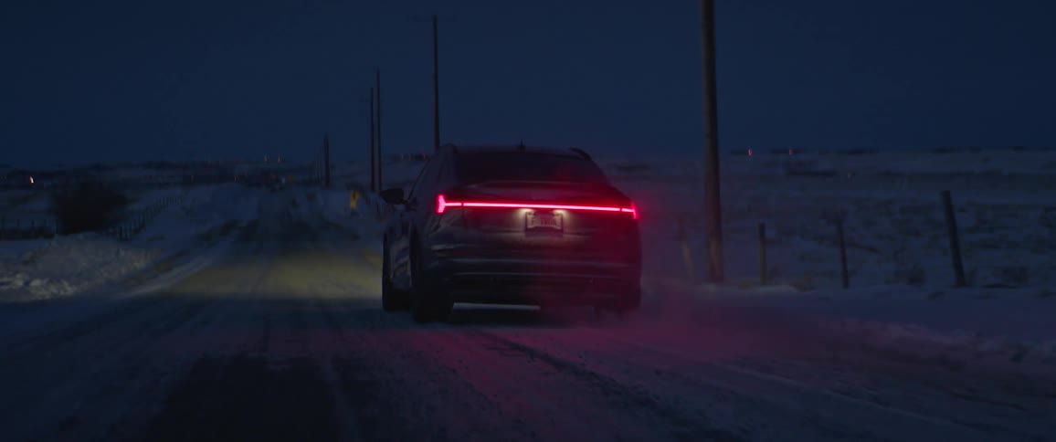 A vehicle driving on a snowy road next to utility poles with the sky and clouds in the background