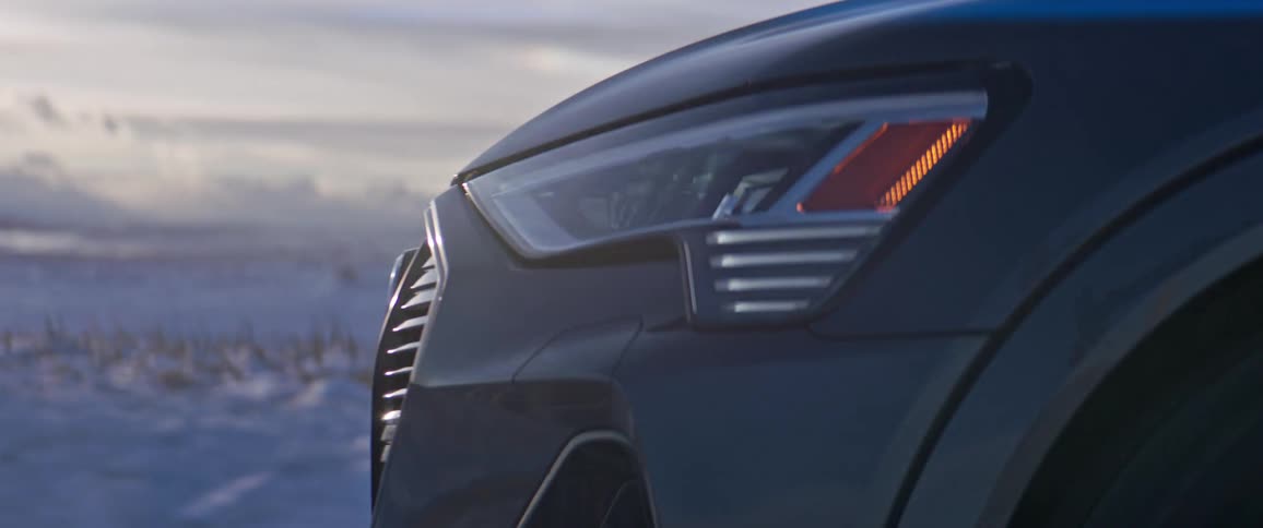 Dark grey audi drives on snowy country road next to farm