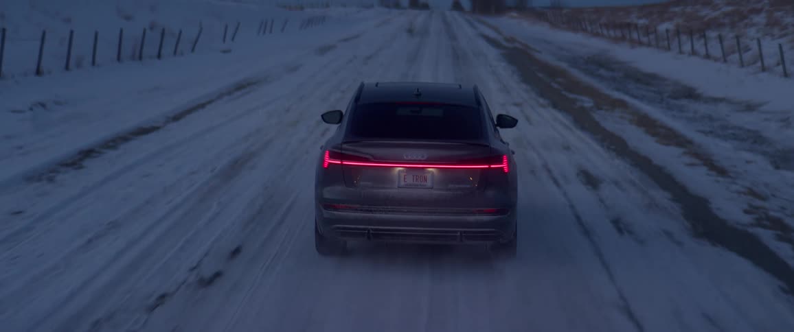 Sedan drives along icy road past snow covered fenced pastures