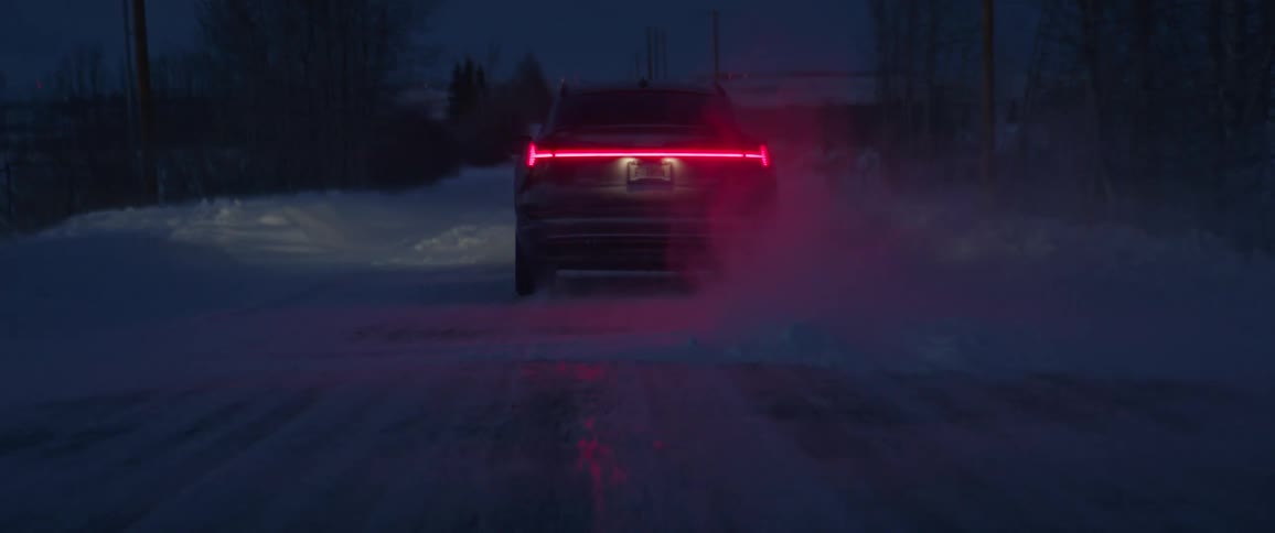 A black car is driving on a road during snowy season