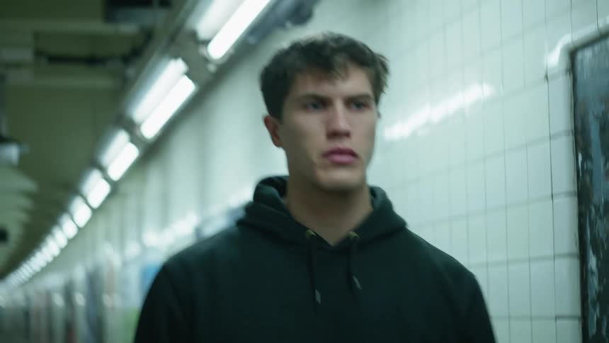 A young male walks alone along an underground subway platform