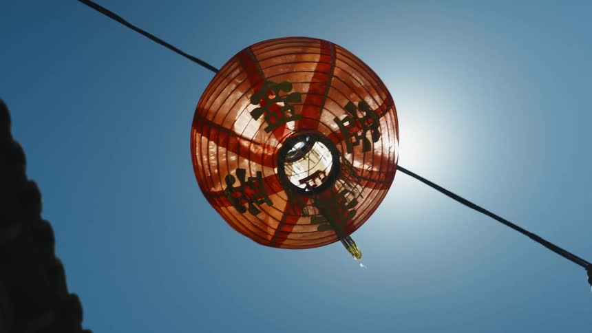 Sunlight filters through an orange round paper lantern hanging from a cable