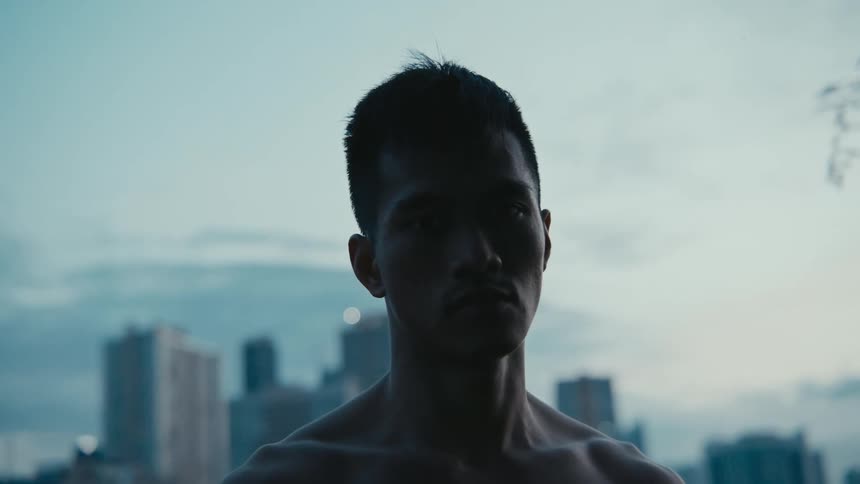 A man standing and staring with buildings the sky and clouds in the background