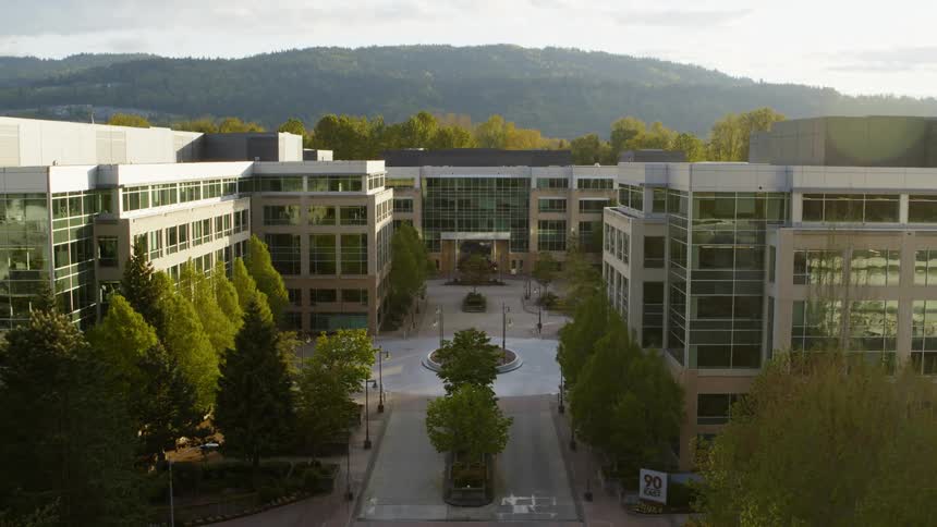 Pullback along a boulevard that leads to a modern office park surrounded by trees and mountains