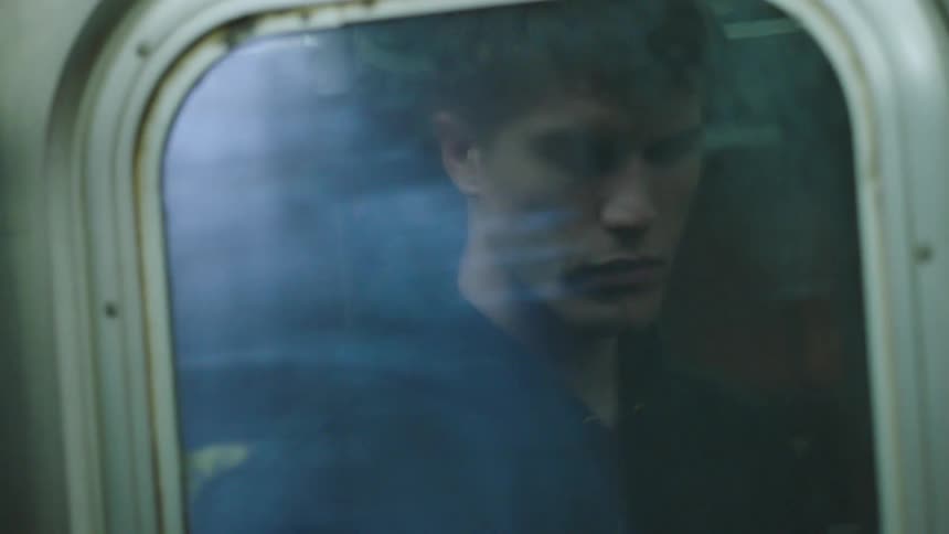 A window shows the reflection of a man in a black sweatshirt on a public train