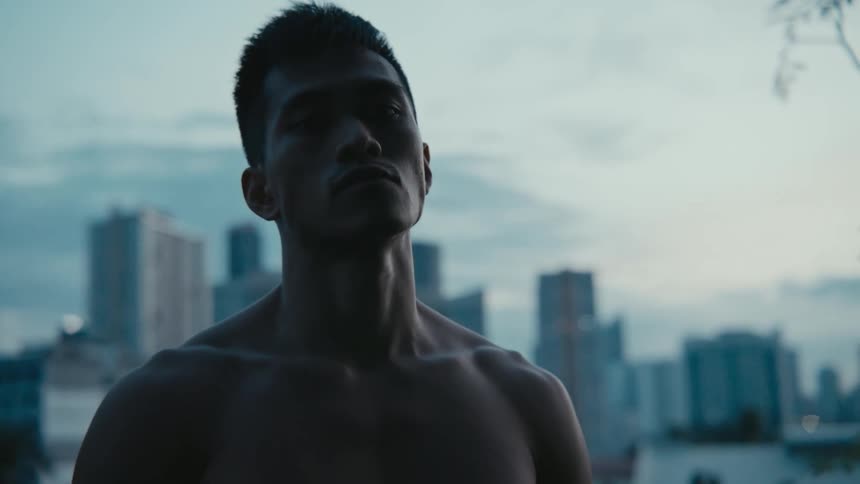 Young shirtless muscular man staring at the camera in front of the city skyline
