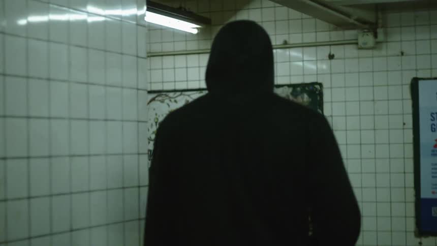 Man wearing a hoodie walking in the tiled subway station