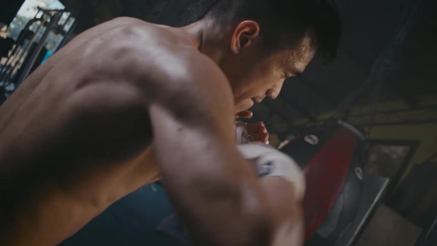 A man in a boxing gym shadowboxing with a heavy bag and equipment in the background