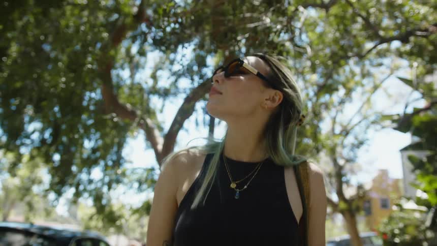 Young woman wearing sunglasses walking under the trees on the city streets