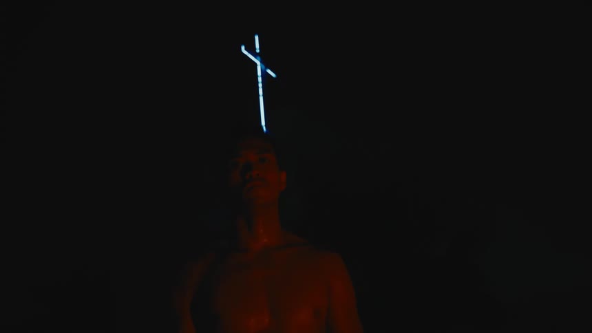 Strong muscular shirtless man standing in front of a cross at night