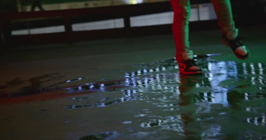 A person dancing on a puddle of water with a billboard and buildings in the background