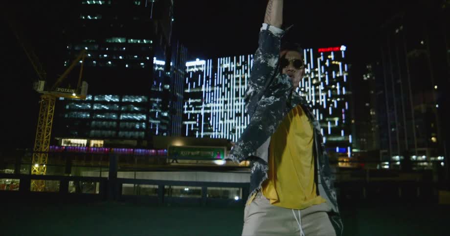 Dancer wearing sunglasses dancing in front of buildings in the city at night while looking at the camera