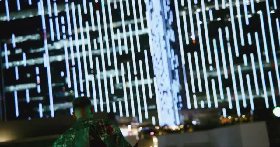 A man with sunglasses dancing with a billboard and buildings in the background