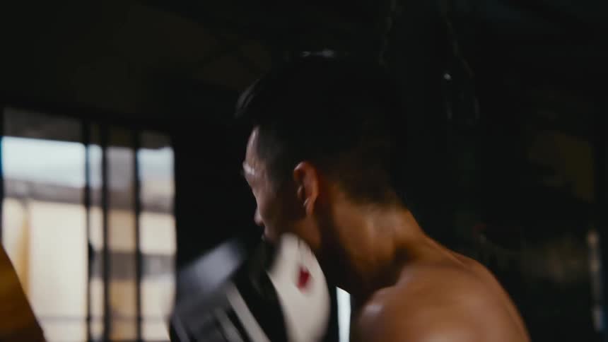 A man with boxing gloves practicing in a boxing gym with a wall and window in the background