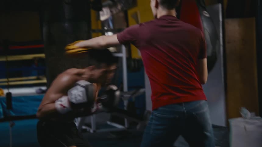 An asian man is practicising boxing with his coach at a gym