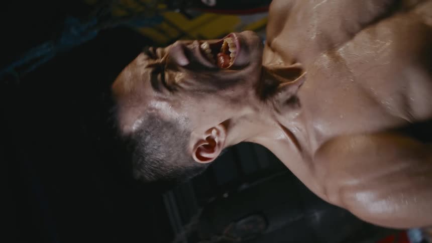 Strong shirtless muscular boxer screams inside a gym