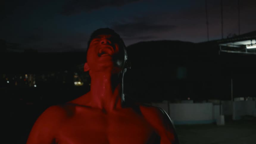 A man on a rooftop screaming with buildings the sky and clouds in the background