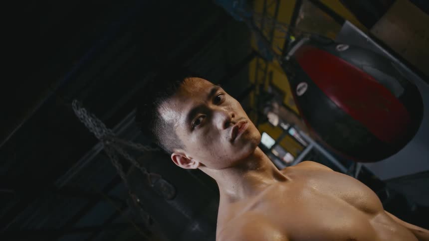 A man stands inside a gym beside a hanging punching bag