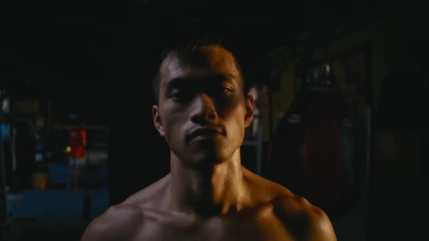 A shirtless man walks slowly through a dimly lit building