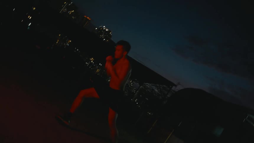 Young muscular shirtless man shadow boxing in front of the camera at night