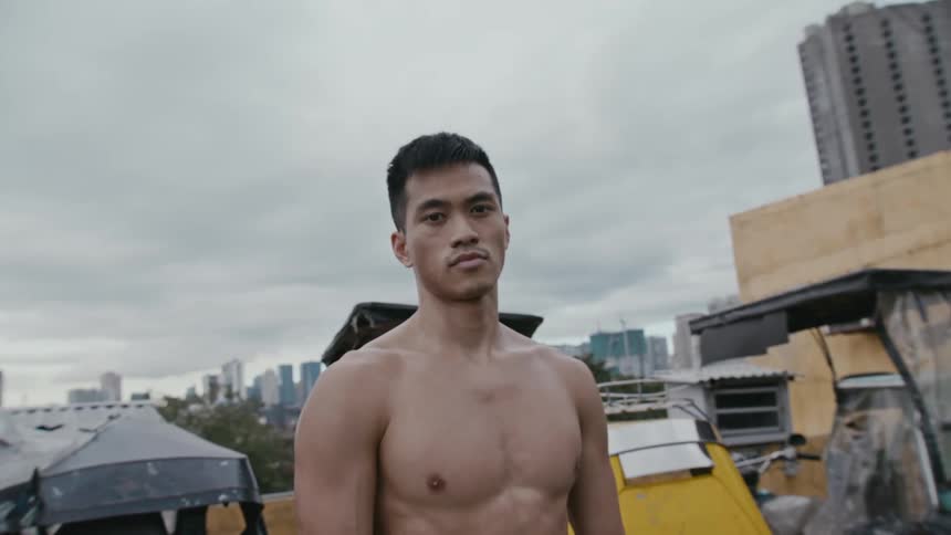A muscular male stands outdoors atop a building in a large city