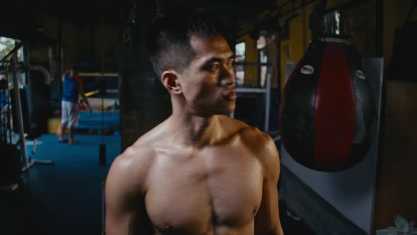 A man walking in a boxing gym with a heavy bag and a boxing ring in the background