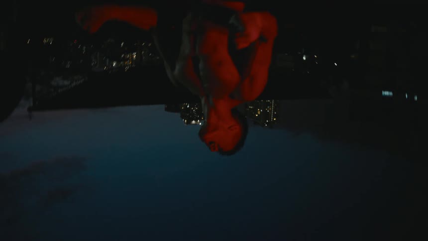 A man standing in front of a city skyline at night clenches his fist and looks up to sky and yells