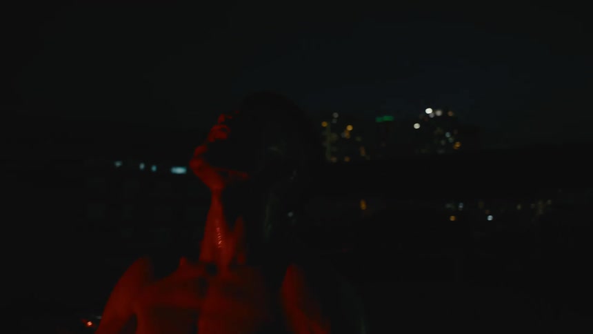 Strong shirtless man screaming at the sky at night in front of the city